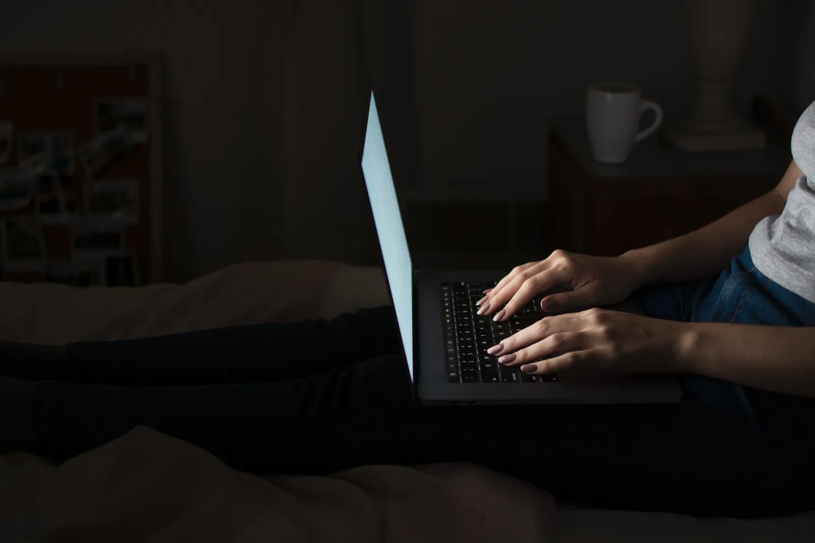 Donna che lavora al portatile di sera al buio, seduta sul letto