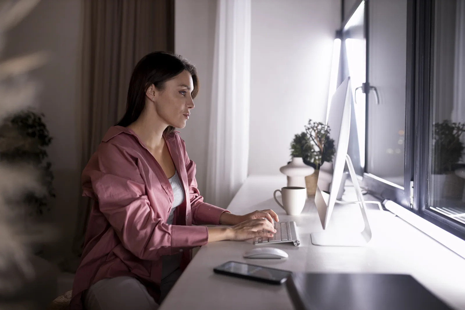 Postazione di lavoro domestica con monitor su supporto, scrivania vicino alla finestra e una persona seduta alla giusta distanza dallo schermo