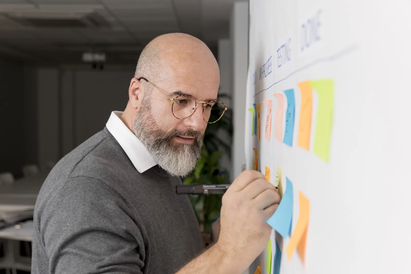 Titolare di una piccola impresa che attacca post-it colorati su una lavagna bianca per pianificare le settimane