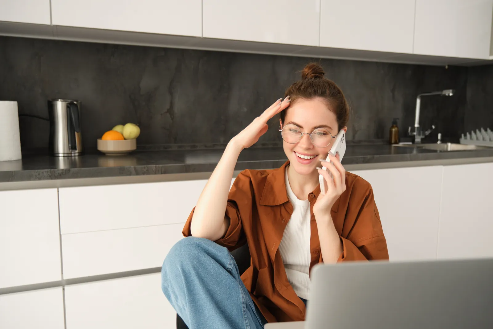 Impiegata in cucina con il portatile aperto che risponde al cellulare sorridendo