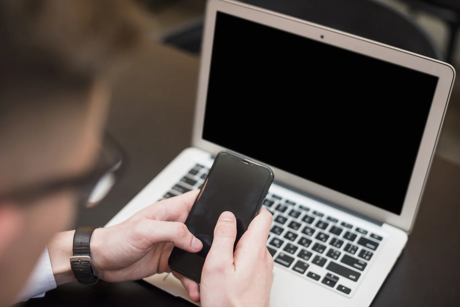 Mano che tiene uno smartphone davanti a un portatile aperto su una scrivania