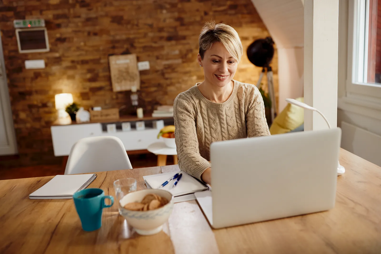 Impiegata sorridente che inizia la giornata di lavoro al portatile sul tavolo di casa