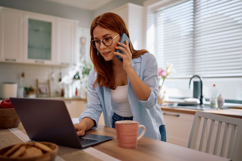 Una professionista lavora da casa al portatile mentre risponde al telefono