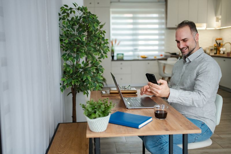 Un dipendente a casa usa lo smartphone alla scrivania con il portatile accanto